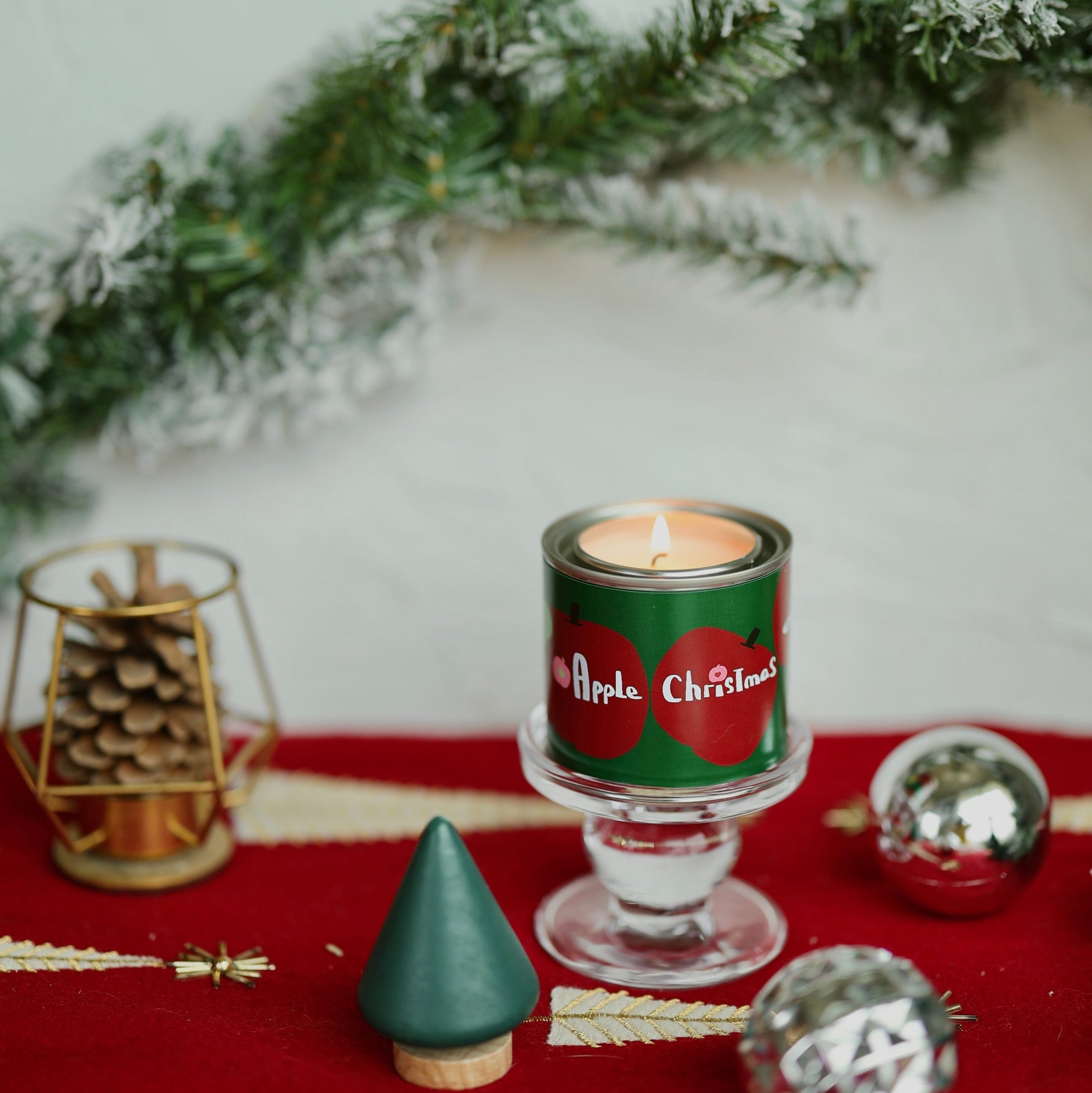 Decorative candle with Christmas design on a red surface with greenery and ornaments.