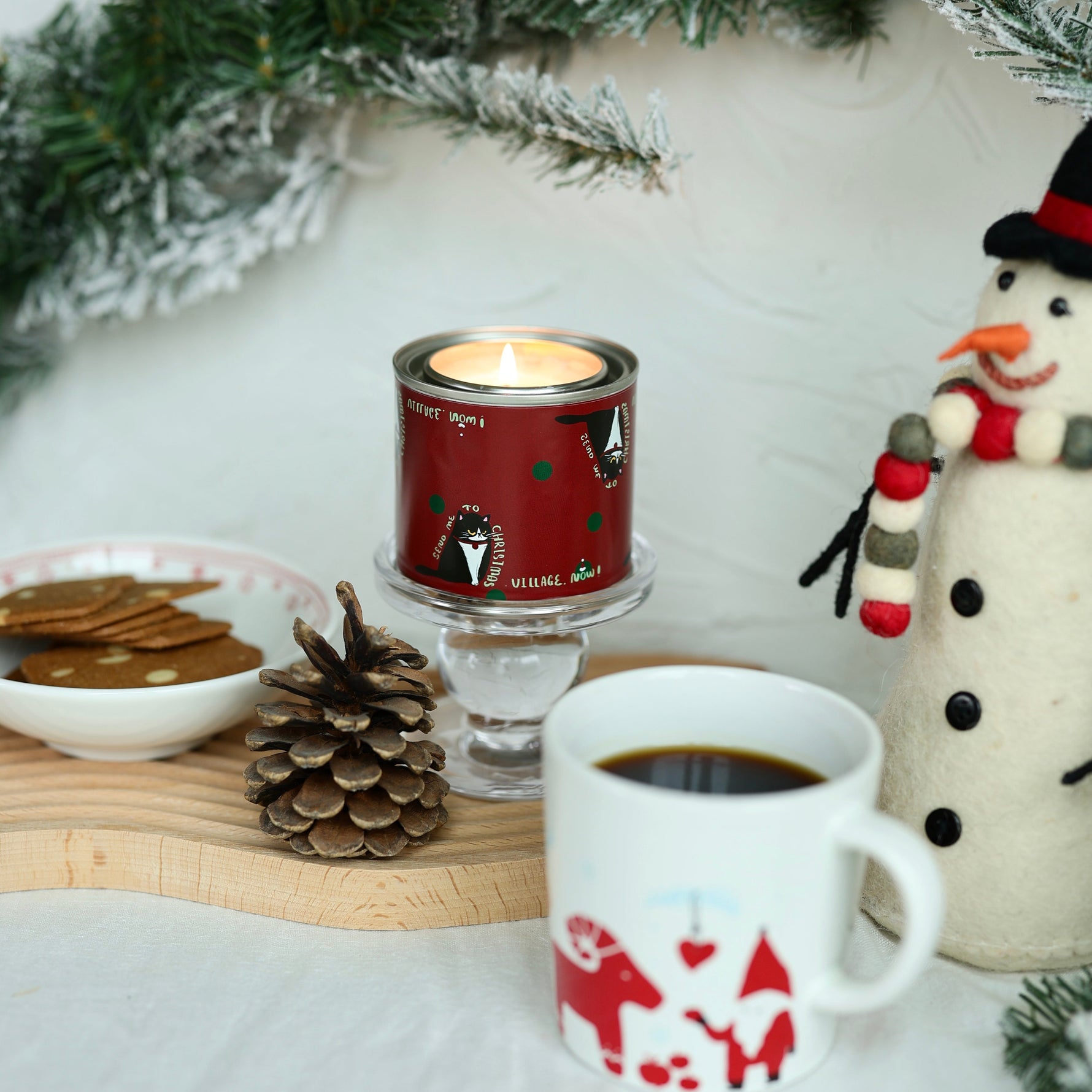 Candle and mug with Christmas design on a table with snowman and pinecones