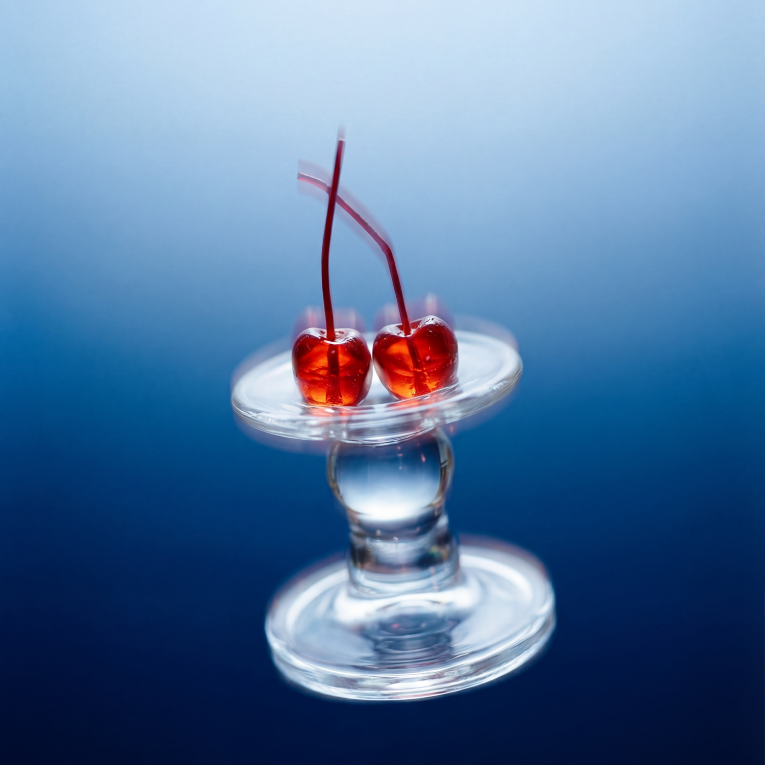 Two cherries on a small glass stand against a blue gradient background